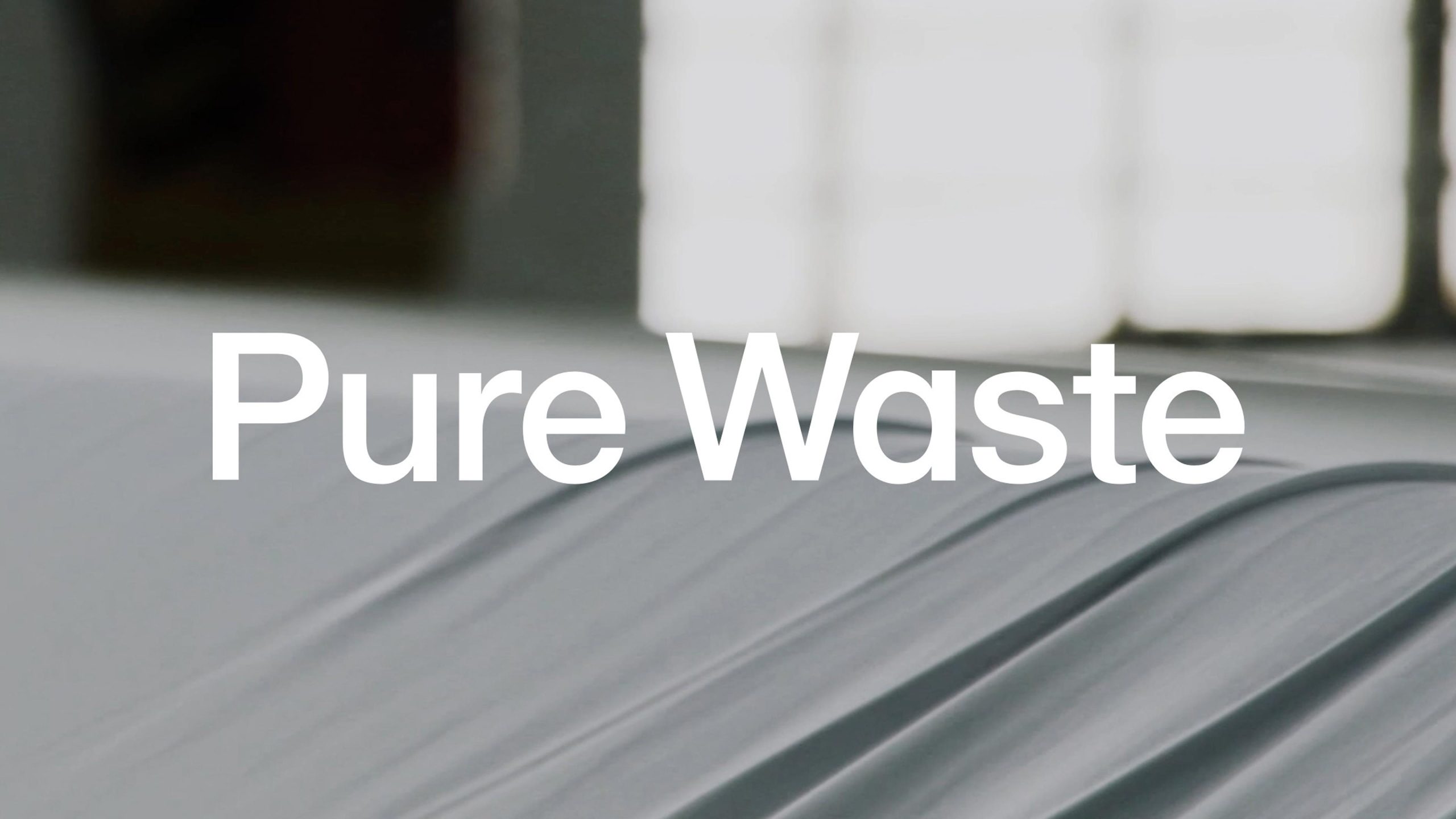 Pure Waste brand title card overlaid on a close-up of grey recycled textile fabric rolls.