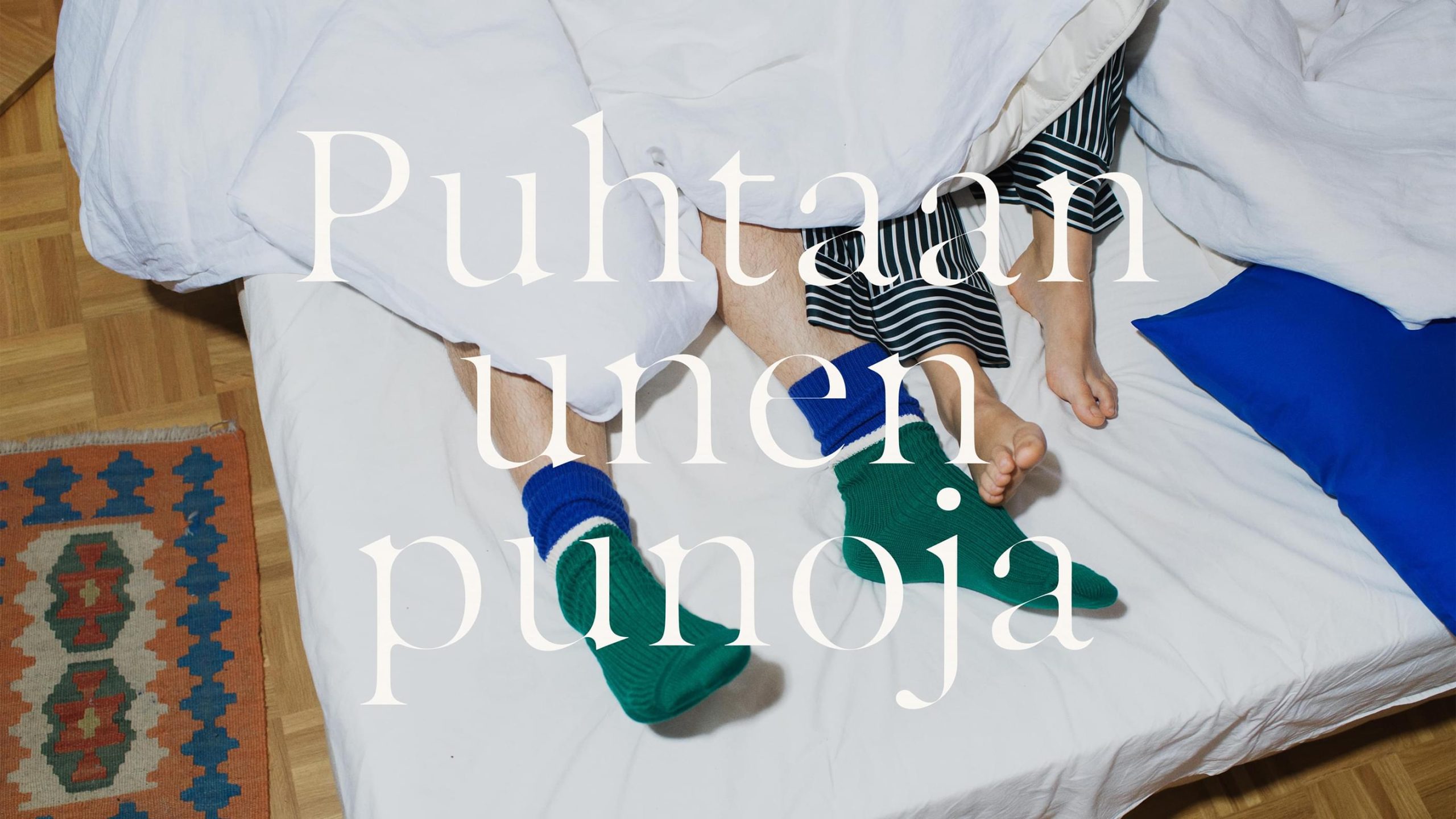 Villa & Peite campaign: two people's feet in green and blue socks on a white bed.