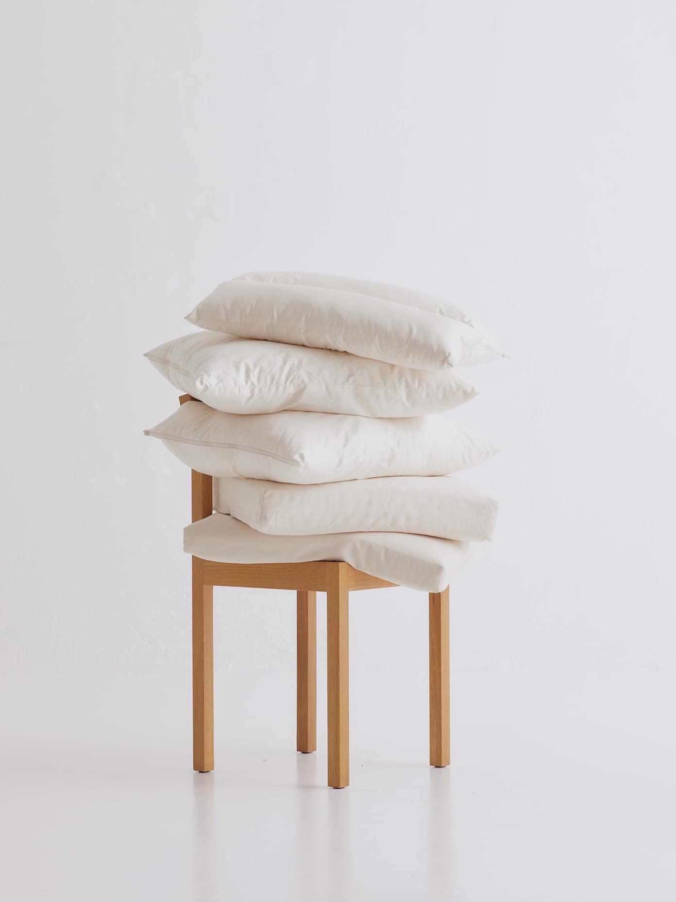 Four white pillows stacked on a natural wood chair against a white background, part of Villa & Peite branding by Werklig.