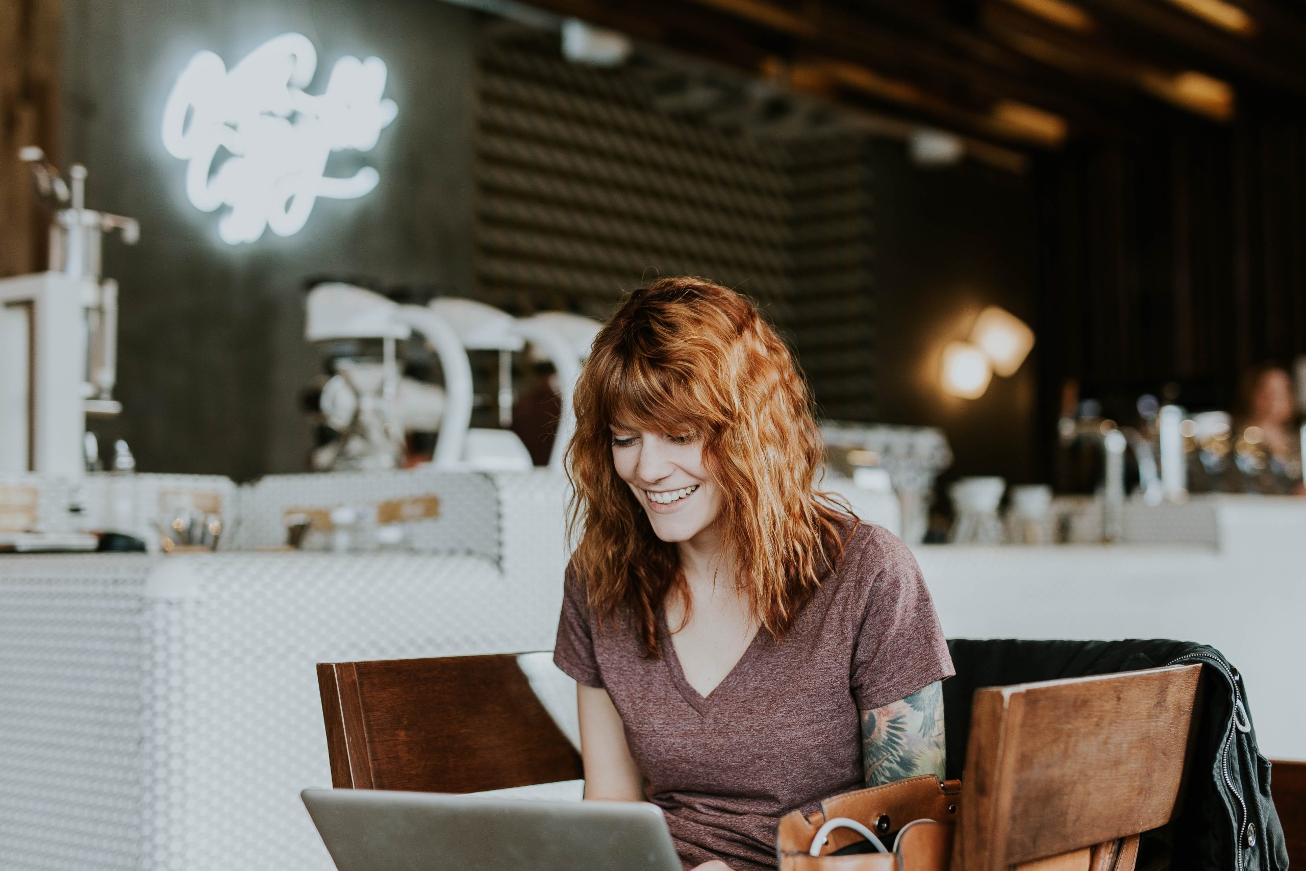 Smiling woman with red hair working on a laptop in a café